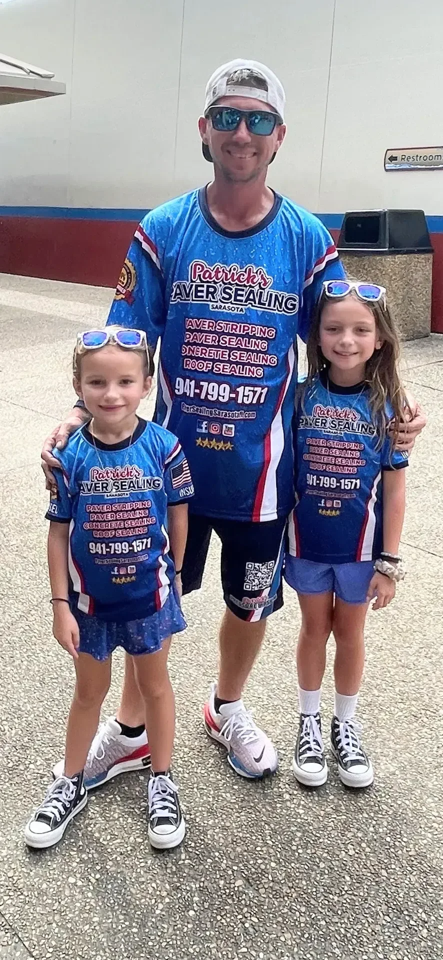 A man standing with two girls, all three in matching blue Patrick's jerseys