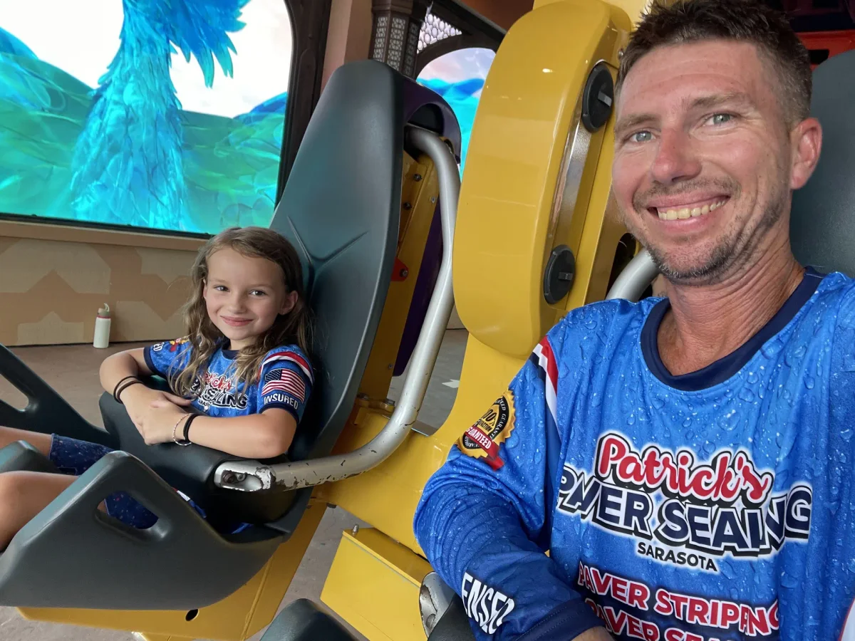 A smiling man in a blue branded jersey taking a selfie, with a smiling girl in a matching jersey sitting beside him