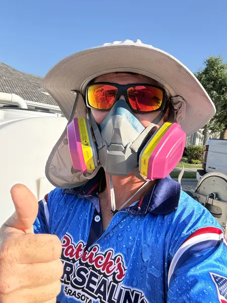 Team member in a sun hat, mirrored sunglasses and a half face respirator giving a thumbs up, in a blue branded shirt with a tank behind