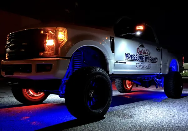 Night view of a lifted white pickup with blue underglow, red wheel lights and Patrick's Pressure Washing door lettering