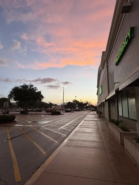 Wide wet sidewalk and parking lane in front of a shopping center at sunset under a pink sky