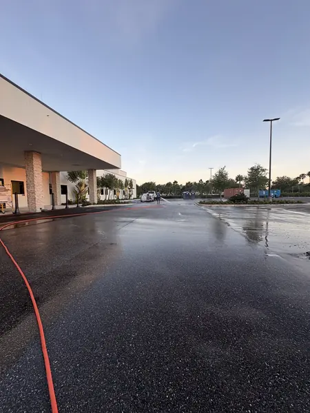 Wet shopping center parking lot and covered walkway at dusk with an orange hose across the asphalt