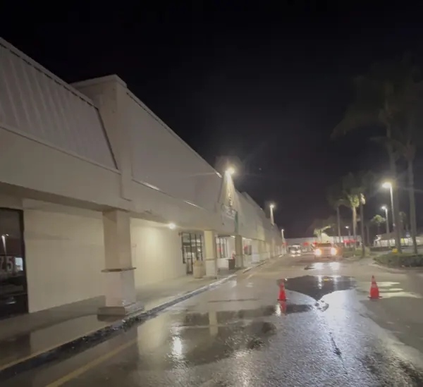 Night view of a long strip mall facade with wet pavement, orange traffic cones and parking lot lights