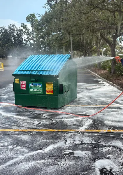 Foam spreading across a parking lot around a green dumpster while a worker's hand sprays with an orange hose