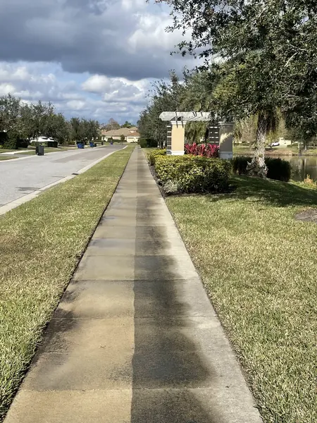 Concrete sidewalk beside a road and pond with the right half darker and stained and the left half lighter