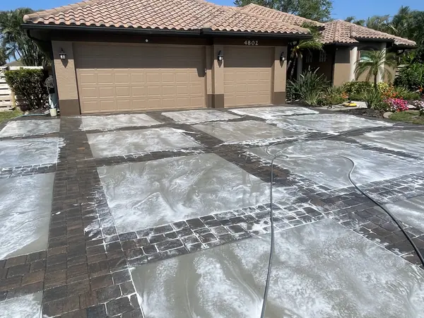 Brick paver driveway with large pale patches of foam or residue in front of a tile roof garage