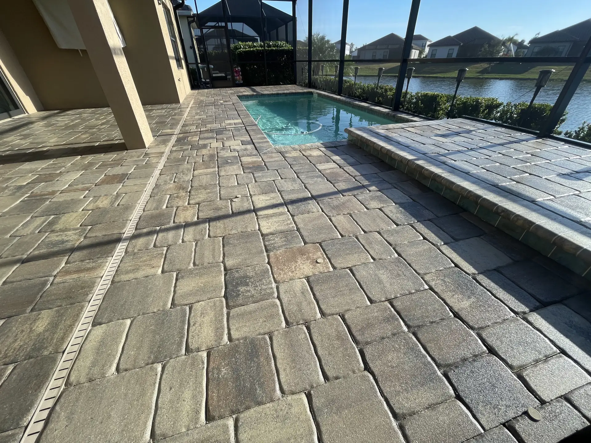 Textured paver pool deck inside a screened lanai with a narrow plunge pool and a lake view