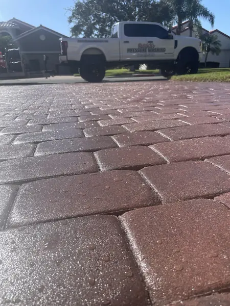 Low angle across wet reddish pavers toward a white pickup truck parked on the street