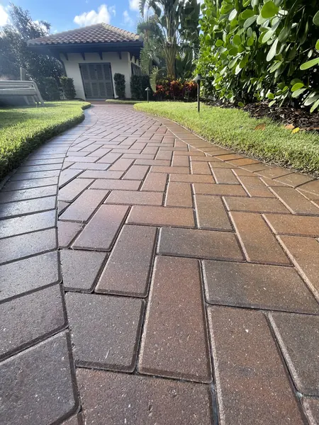 Brick paver walkway curving beside a lawn toward a house entrance