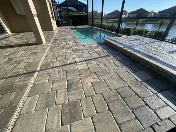 Textured paver pool deck inside a screened lanai with a narrow plunge pool and a lake view