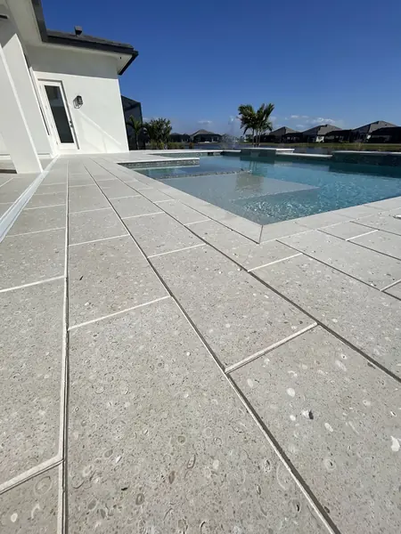 Large light gray pavers around a pool beside a white house, clean and even