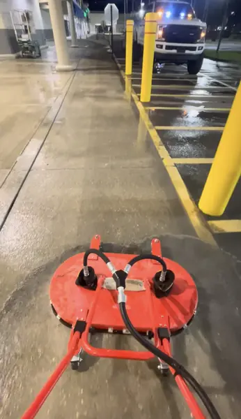 Red twin head surface cleaner on a wet concrete walkway beside yellow parking bollards at night