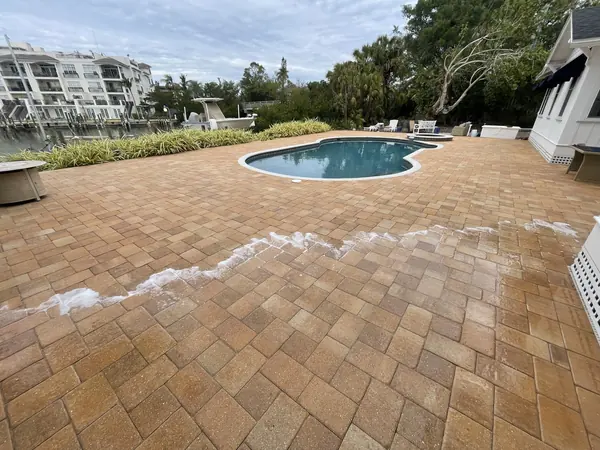 Brick paver pool deck with a foam line moving across the surface, a pool and waterfront buildings behind