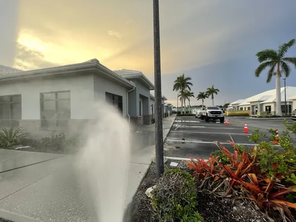 Pressure washer spray rising beside a stucco commercial building at dusk with a truck and cones in the lot behind