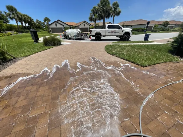 Detergent foam spreading in a wavy line across a brick paver driveway with the work truck and trailer on the street