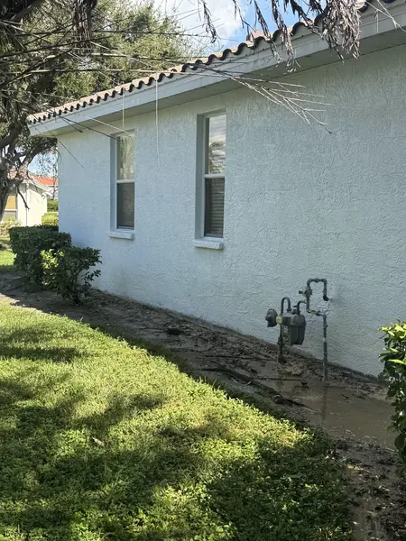 The same stucco wall after washing, white and even with the orange staining gone and wet ground below