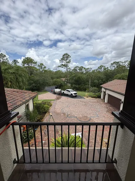 View from an upper balcony down to a paver driveway with ladders, hoses, and a pressure washing truck on the road