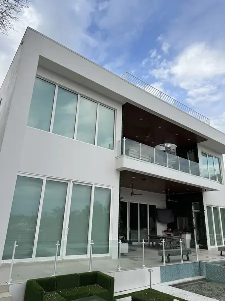 Modern white two story house with large glass windows and balcony railings under a blue sky