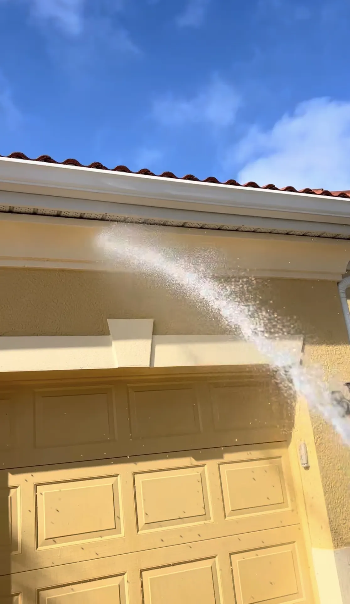 Water arcing up under the roof edge above a yellow garage door, with the gutter line along the eave