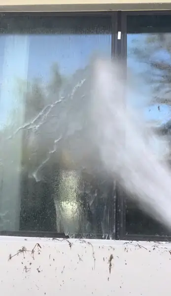 High pressure water spraying across dirty window glass with mineral streaks and spots visible