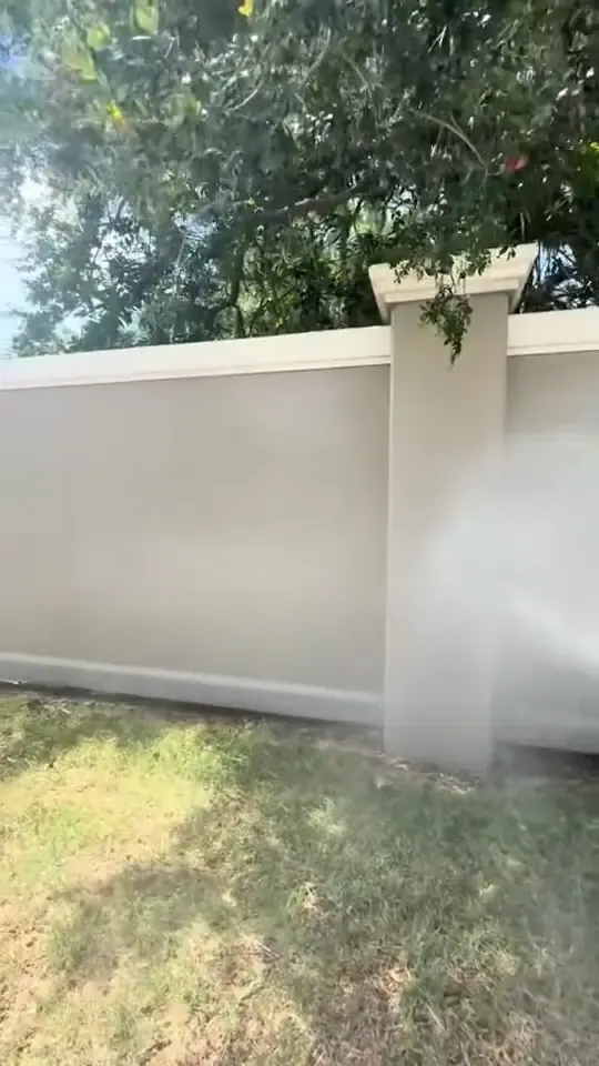 Washing algae and dirt off a long stucco perimeter wall beside a road.