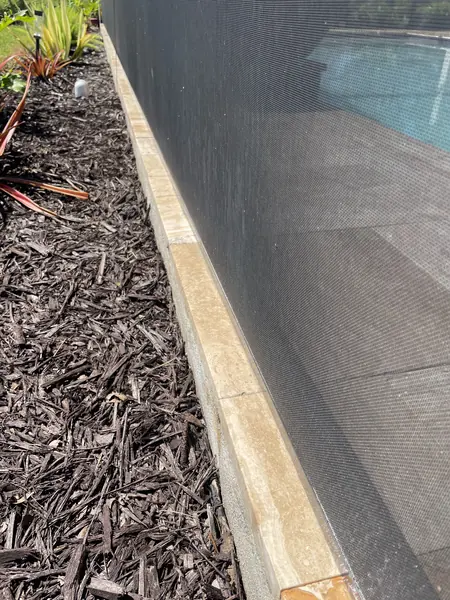 Warmer toned stone coping strip between a mulch bed and a dark pool screen, same view as the before shot