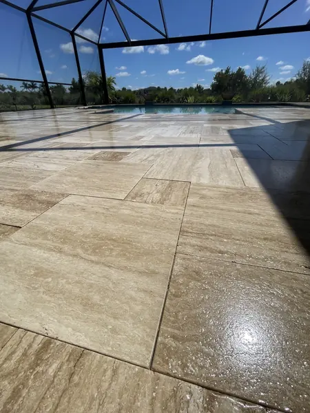 Low view of honed travertine floor in a screened pool enclosure with a glossy wet patch in the foreground