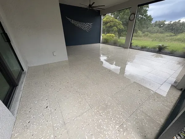 Covered lanai with a speckled shell aggregate tile floor, wet and glossy on the right, screen wall and garden beyond