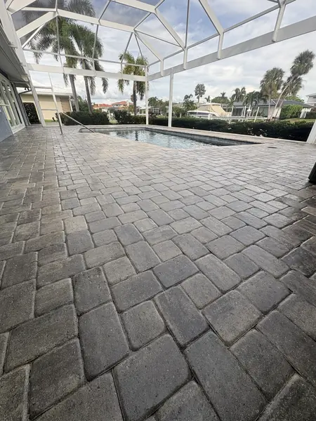 Wide low view of a screened pool lanai with a gray tumbled paver deck and a small pool beyond