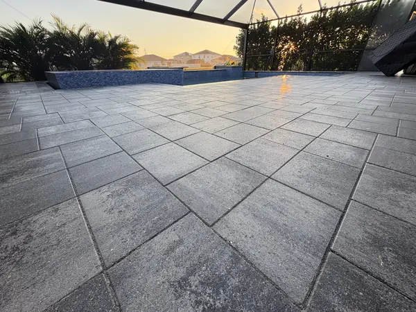 Large format gray paver pool deck inside a screen enclosure at dusk, with a raised spa wall in the background