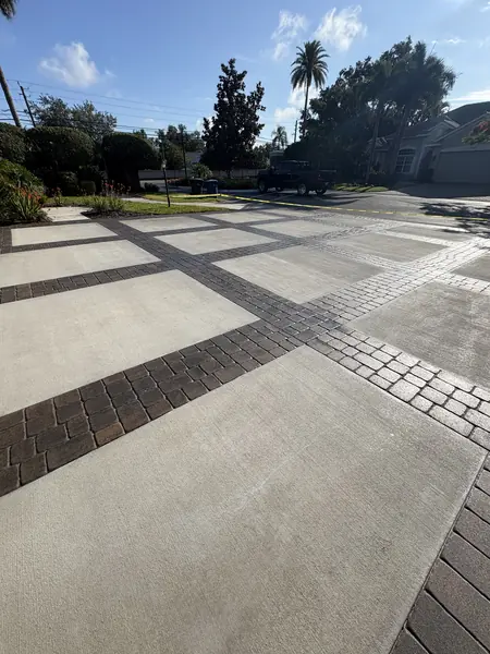 Concrete slab driveway divided by dark brick paver bands, with caution tape and a parked pickup near the street