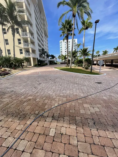 Large circular paver drive at a high-rise condo with a hose running across it and palm trees against a blue sky
