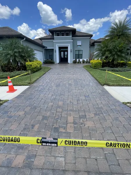 Gray-brown paver driveway leading to a modern gray home, with caution tape and a company sign hanging across the foreground