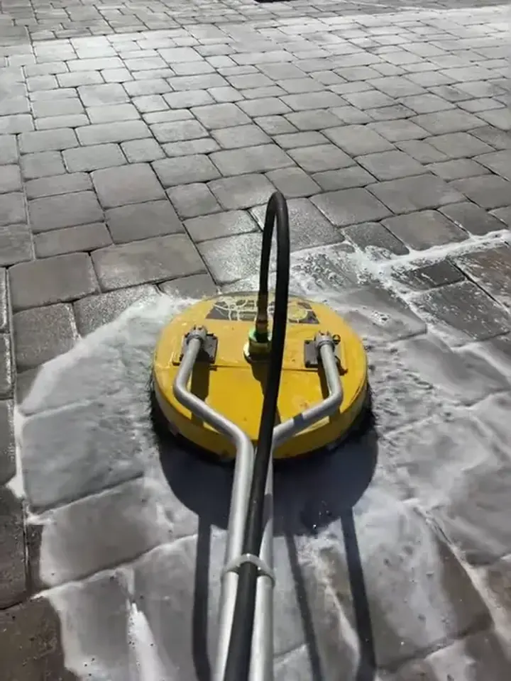 A dull tan paver driveway scrubbed with a yellow surface cleaner.