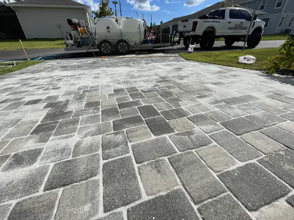 Light gray paver driveway with fresh joint sand swept across it and a work truck with a wash trailer in the background