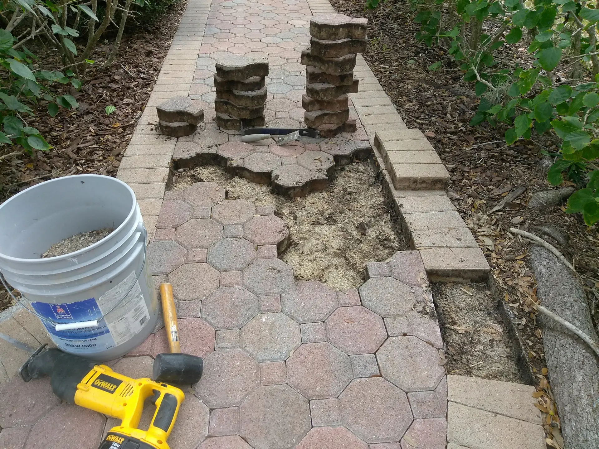 The octagon paver walkway with a section lifted and stacked, a mallet, bucket and tools beside it
