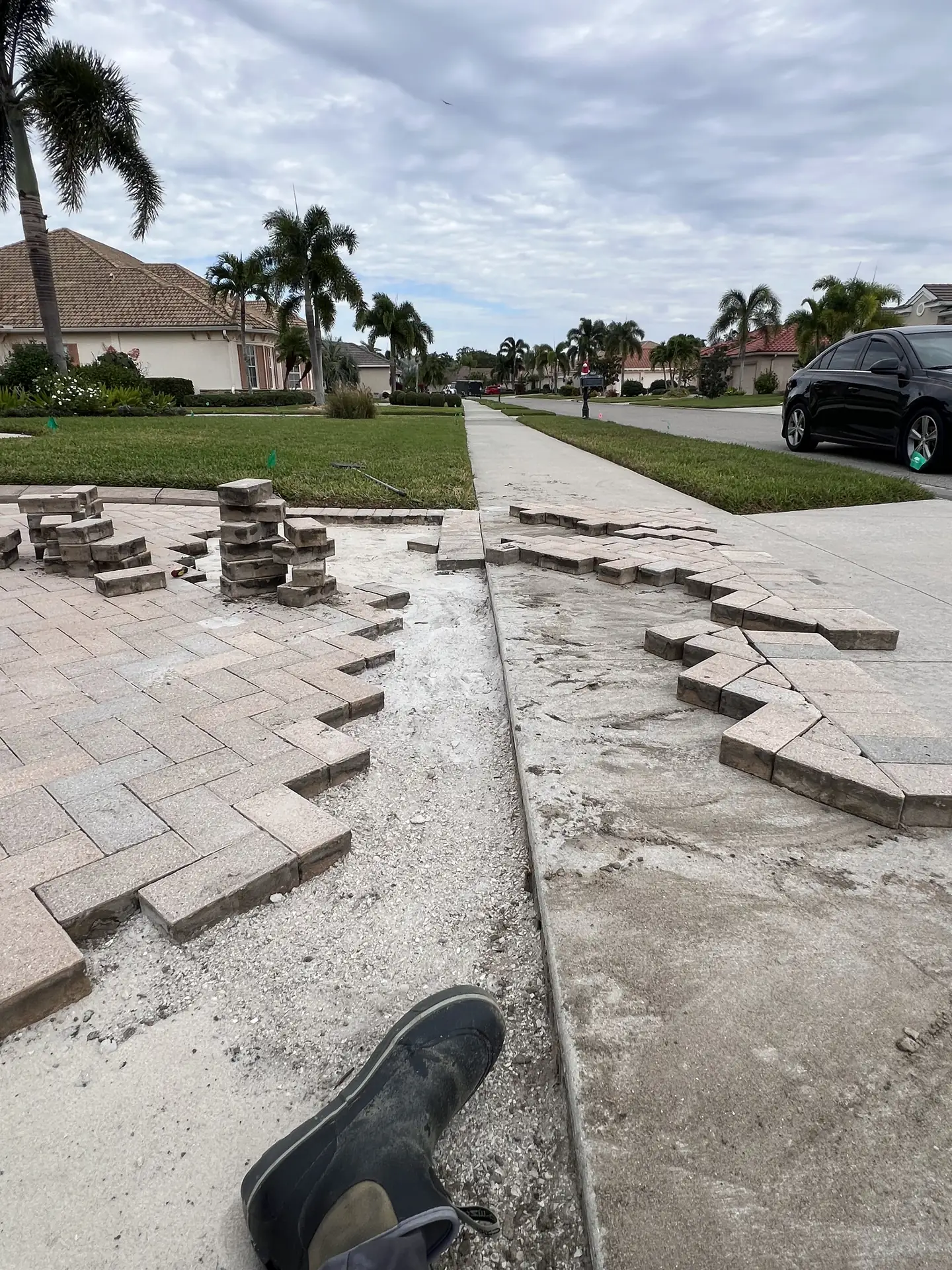 Driveway apron with pavers removed in a zigzag, stacked pavers and a screeded base, and a work boot in the foreground