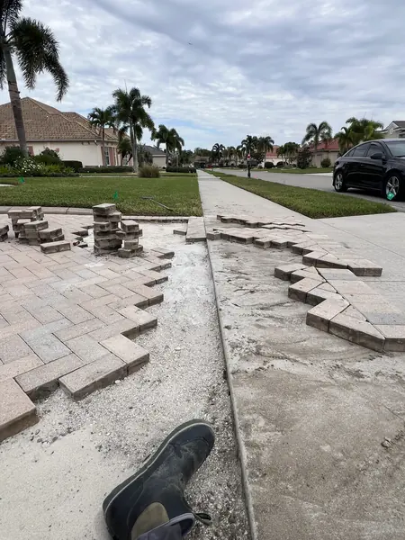 Driveway apron with pavers removed in a zigzag, stacked pavers and a screeded base, and a work boot in the foreground