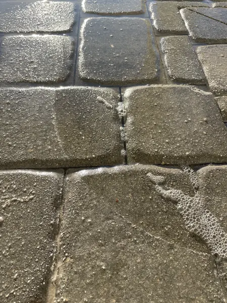 Close-up of wet tumbled pavers with bubbles of foam gathered in the joints