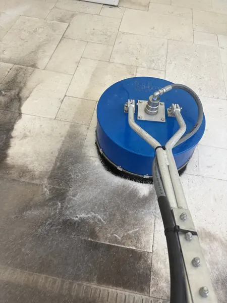Blue rotary surface cleaner on a cream stone tile pool deck, lifting dark dirty streaks from the surface
