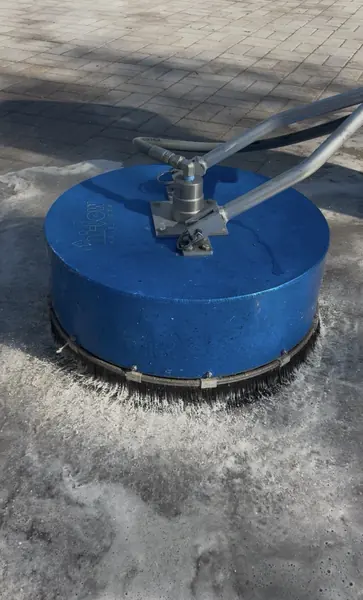 Blue rotary surface cleaner on dark gray pavers with a ring of foam around the brush