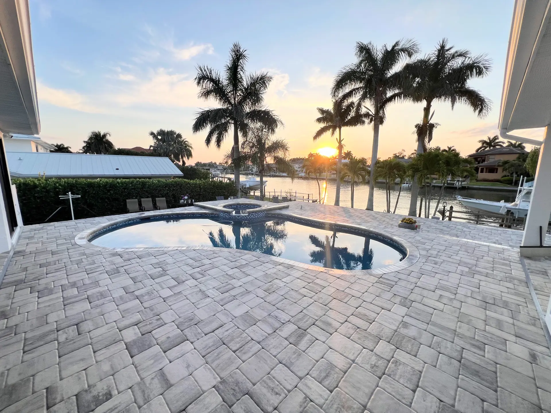 Brick paver pool deck at sunset with a kidney shaped pool, palms and a waterway behind
