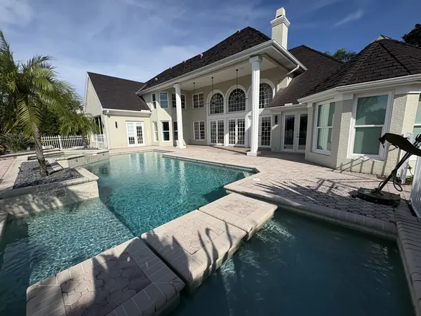 Rear of a large home with a pool, octagon pavers and a rotary surface cleaner parked at the right edge