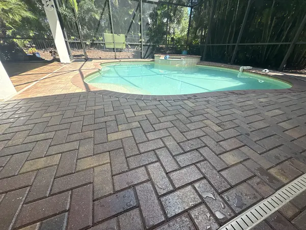 Herringbone brick paver pool deck inside a screen enclosure with a drain channel, pool at the back