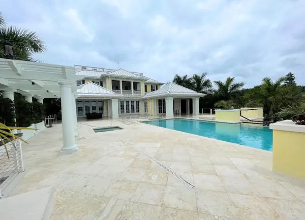 Large pale travertine pool deck in front of a two story home with a white pergola and metal roof
