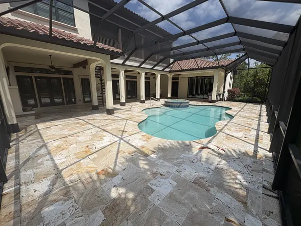 Travertine pool deck inside a large screen enclosure, pool and spa beyond, seen from the covered lanai