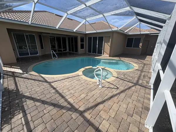 Paver pool deck in a white framed screen enclosure, foamy streaks on the roof panels, a home behind